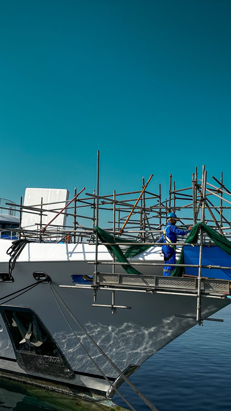Technician working from scaffolding alongside a yacht