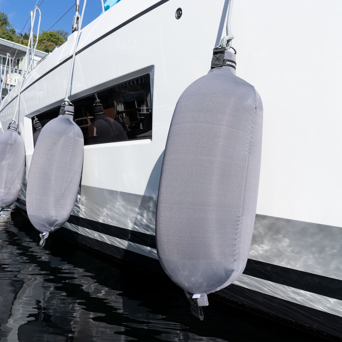 Fendertex textile fenders hanging from the side of a superyacht moored at a dock