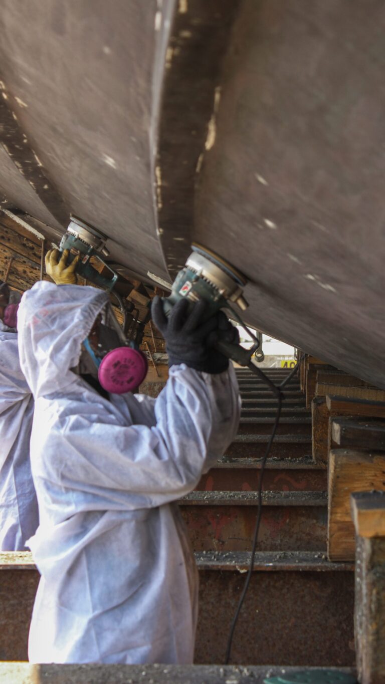 Hull surface preparation by a technician wearing protective equipment